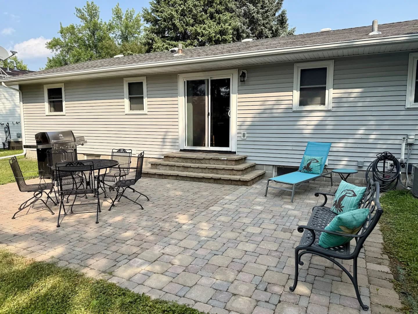 Backyard paver patio with a grill, outdoor dining table, bench, and lounge chair
