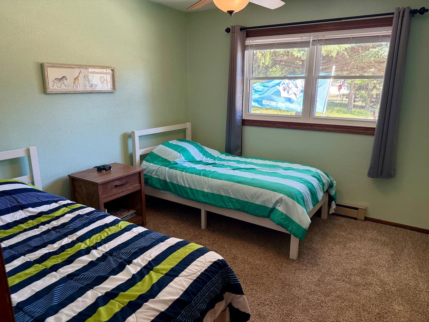 Two twin beds with striped quilts beside a window with blackout curtains