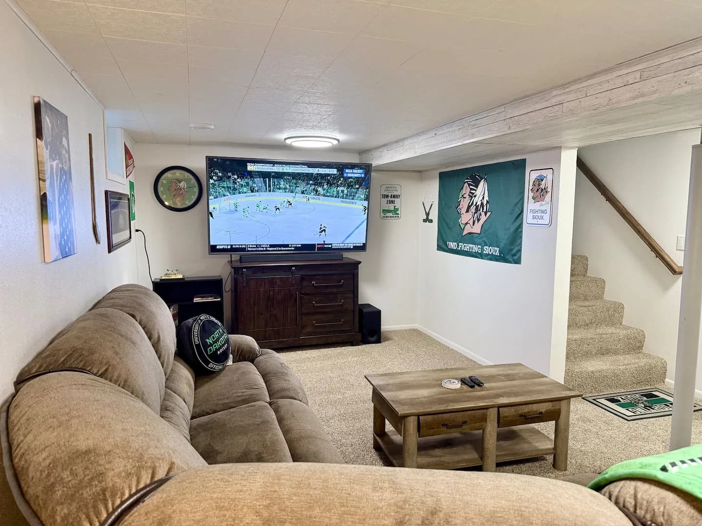 Basement family room with a sectional sofa, coffee table, hockey decor, and a large TV showing a game